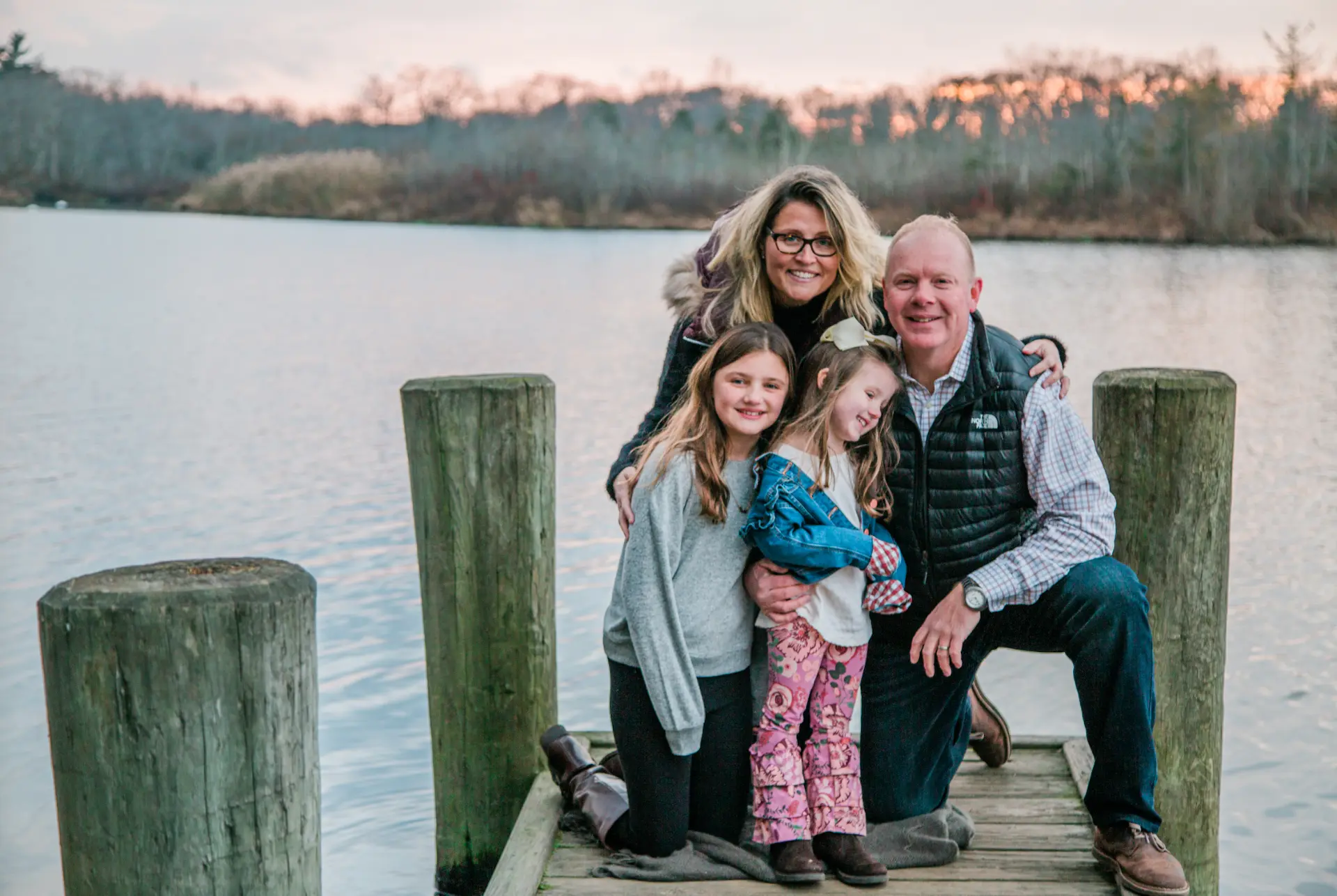 Family of four on a wooden dock at sunset on a lake