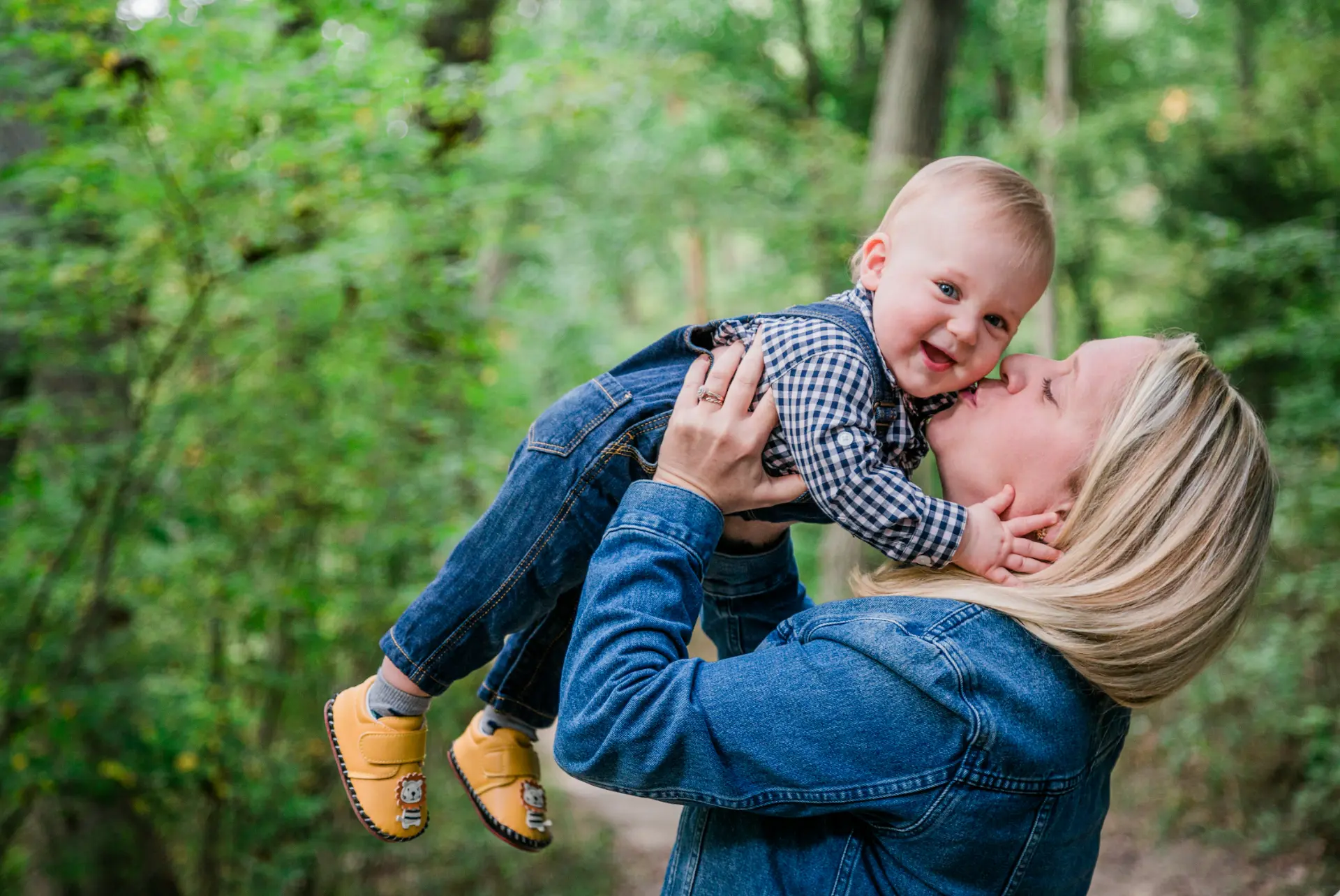 Mother lifting and kissing her baby boy on a wooded trail