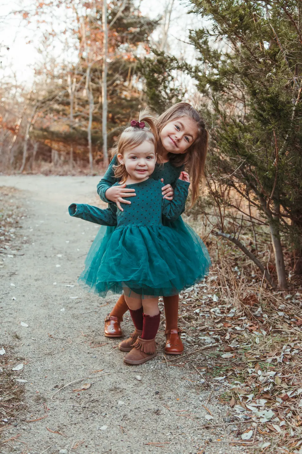 Two sisters in matching teal tulle dresses hugging on a sandy trail