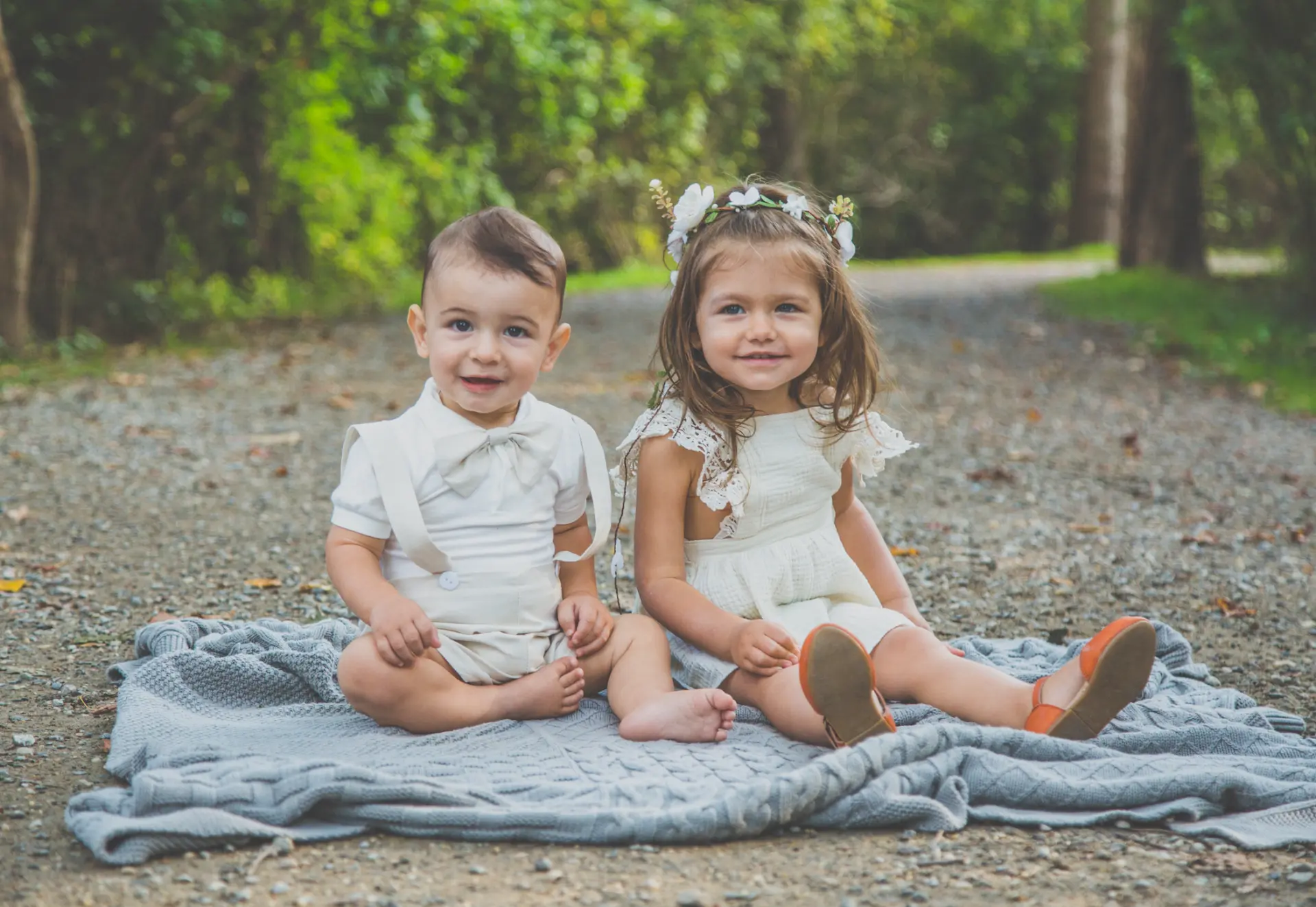 Two toddlers in cream outfits sitting on a knit blanket outdoors