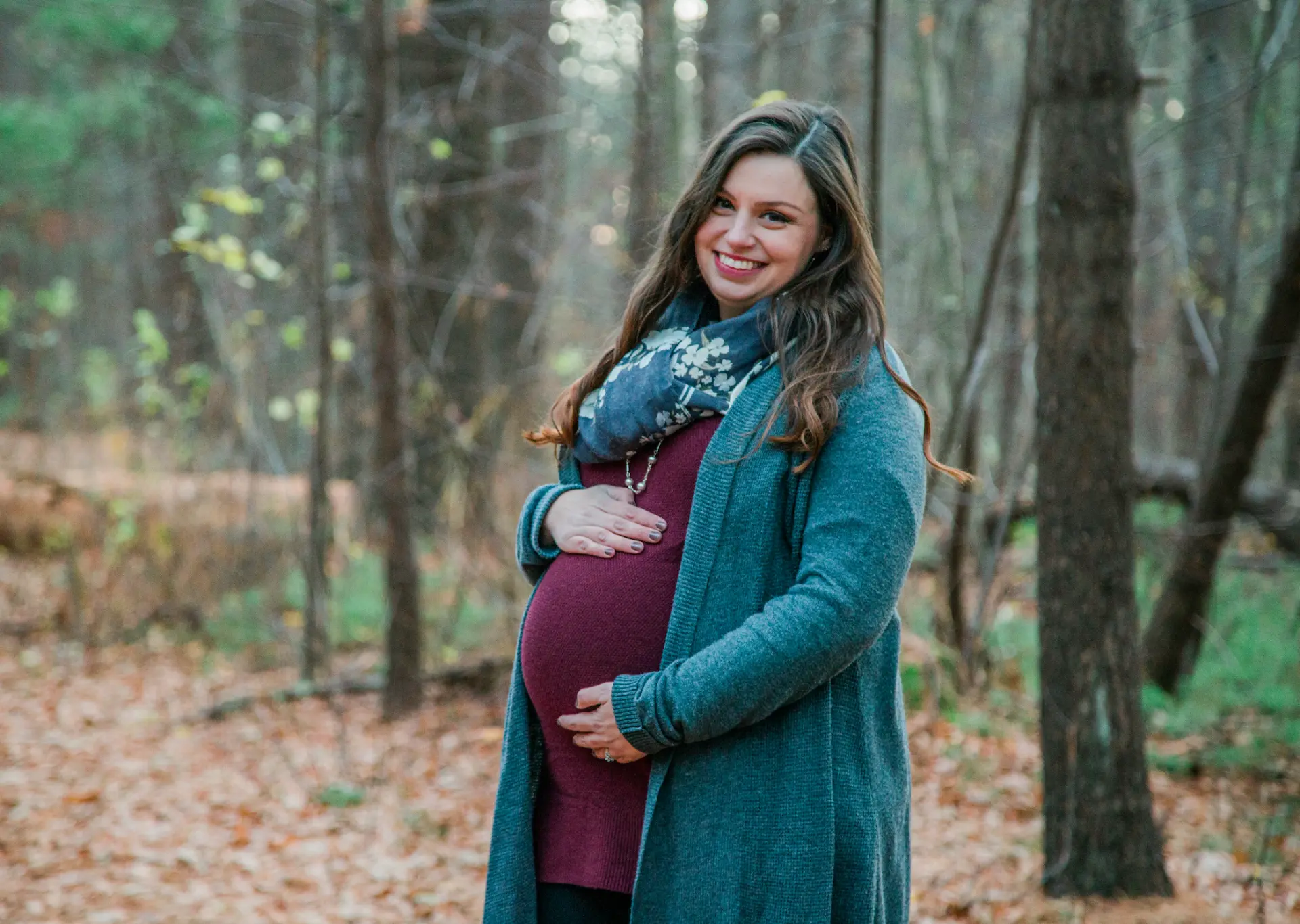 Maternity portrait in a burgundy dress and teal cardigan in the woods